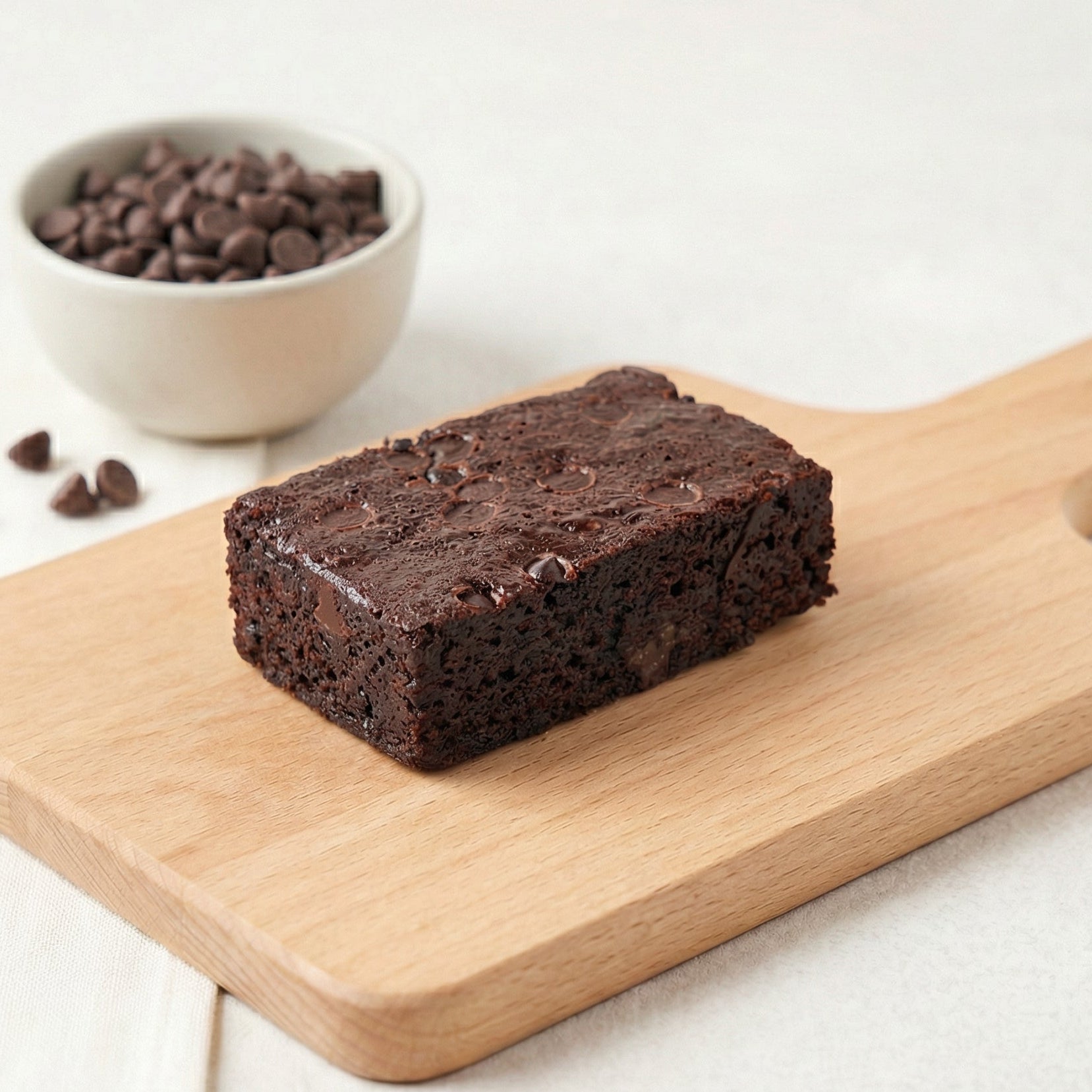 Chocolate chip brownie on wooden board with chocolate chip bowl