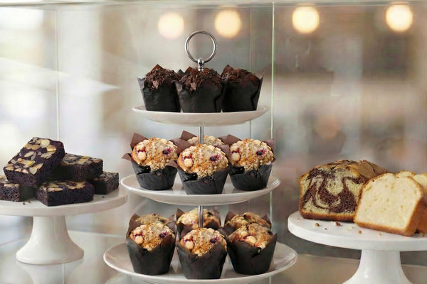 Three-tiered dessert display with blueberry and chocolate muffins, brownies, and individual butter cake slices.