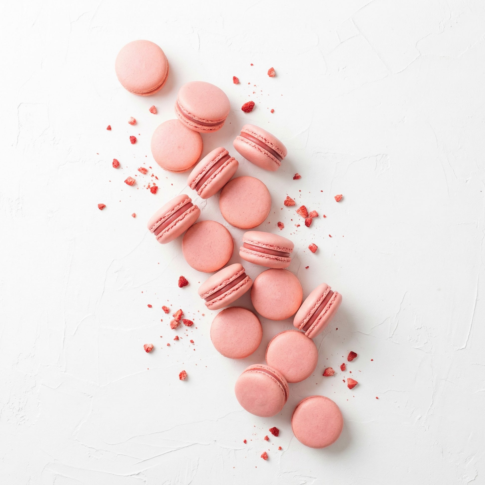 Strawberry macarons on a white surface with real strawberries.