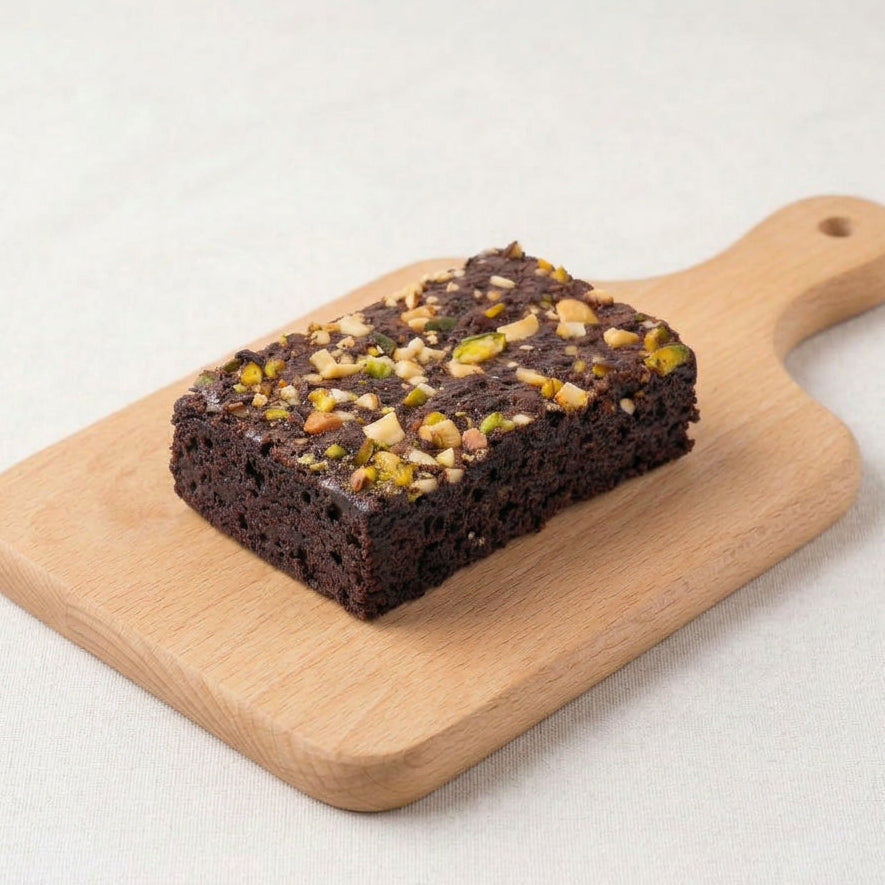 Chocolate brownie with cashew nuts and pistachio on a wooden cutting board