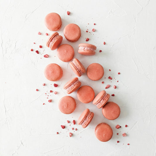 Strawberry macarons on a white surface with real strawberries.